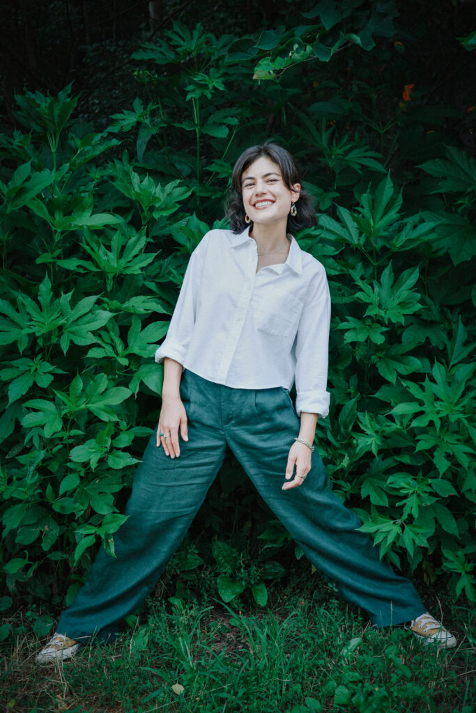 Photograph of Tara smiling and standing in front of a wall of leaves